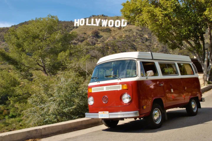 A vintage red & white VW bus, reminiscent of an RV rental, parked near the iconic Hollywood sign on a sunny day.. Volkswagen Westfalia 1978