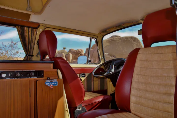 Inside a retro VW camper van, an inviting RV rental for desert adventures. Red/tan seats, wood interior, and a view of rocky terrain.. Volkswagen Westfalia 1978