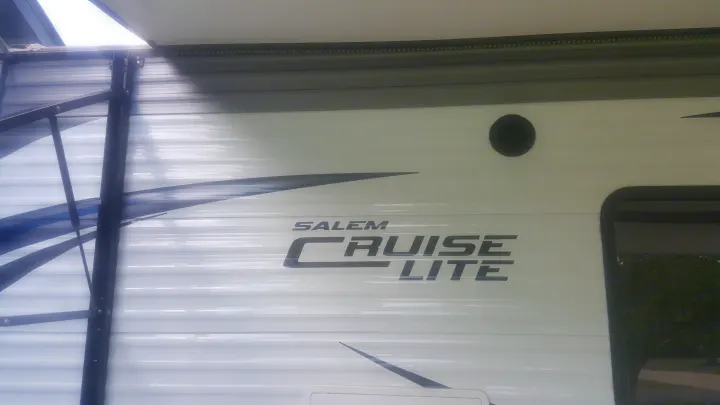 Side view of a white Salem Cruise Lite travel trailer RV rental, featuring an extended awning and circular vent.. Forest River Salem Cruise Lite 2017