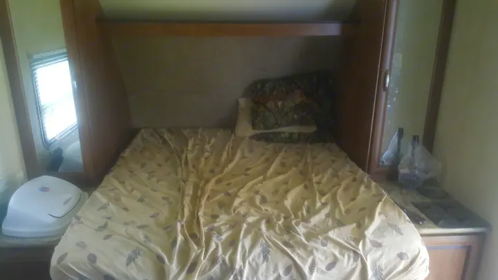 Cozy RV rental bedroom with a patterned bed, overhead storage, and bedside table, offering a comfortable sleeping area.. Forest River Salem Cruise Lite 2017