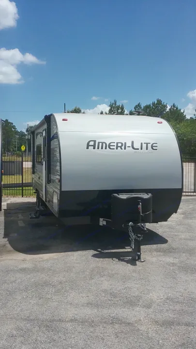 A white Ameri-Lite travel trailer by Gulf Stream, ideal for RV rental adventures, parked outside under a clear blue sky.. Gulfstream 248BH 2018