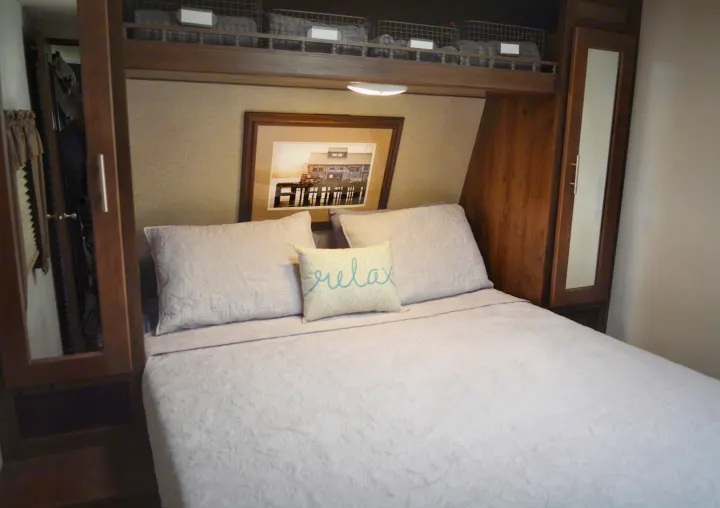 Cozy RV rental bedroom features a comfy bed with "relax" pillow, built-in storage, and decorative picture.. Forest River Wildcat Maxx Lite 2018