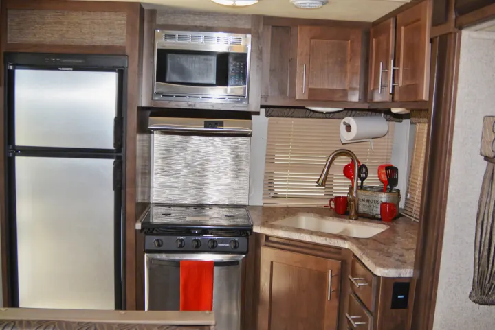 Compact RV rental kitchen, featuring a full fridge, microwave, stove, and sink with ample cabinet space.. Forest River Wildcat Maxx Lite 2018