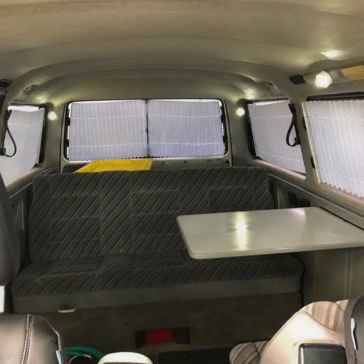 RV rental interior: striped bench seat, folding table, and pleated window blinds provide comfort and privacy.. VW Wolfsburg 1989