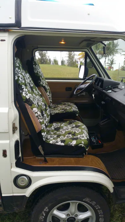 This RV rental's interior features tropical floral seat covers, steering wheel, dashboard, and a view of palm trees outside.. VW Westfalia 1986