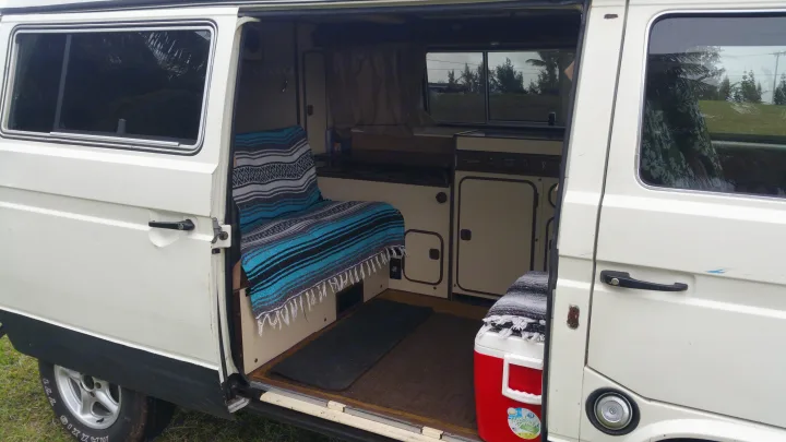 White camper van RV rental with open side door revealing a compact interior, ideal for adventurous road trips.. VW Westfalia 1986
