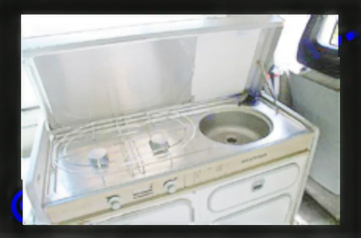 This RV rental's compact kitchen unit features a two-burner stove, sink, and storage cabinets, ideal for camping.. VW Westfalia 1990