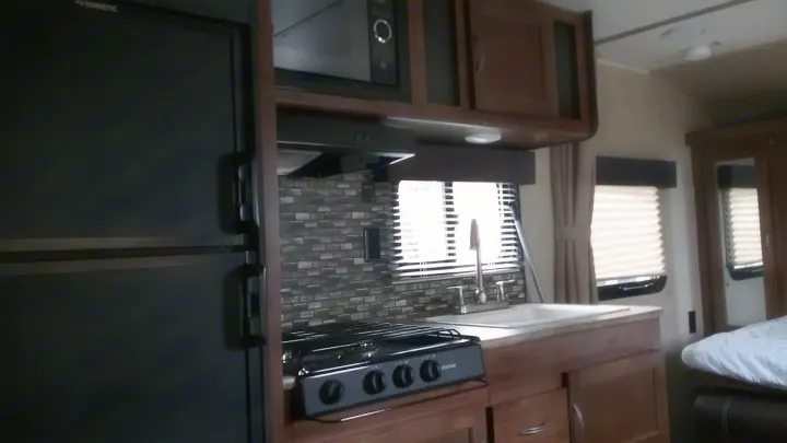 RV rental interior featuring a compact kitchen with refrigerator, microwave, stove, sink, and wood cabinets.. Gulfstream 248BH 2018