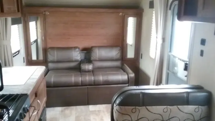 Spacious RV rental interior with a brown reclining sofa, wooden wall, mirrors, kitchen counter, and bright windows.. Gulfstream 248BH 2018
