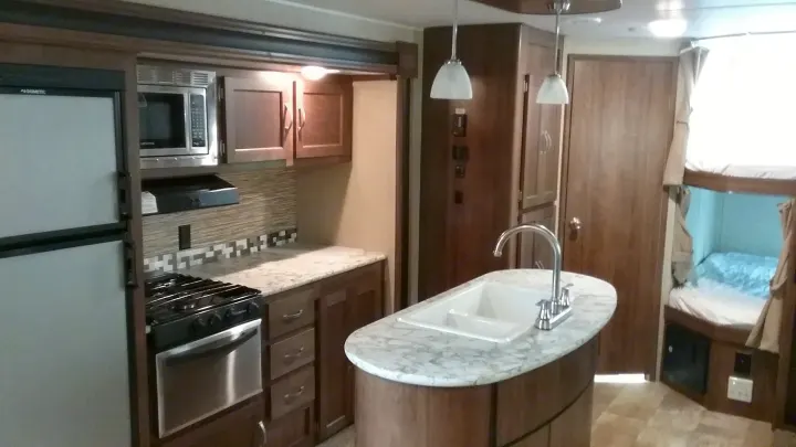 Spacious RV rental interior featuring a modern kitchen with a large fridge, stove, microwave, island sink, and cozy bunk beds.. Gulfstream 288ISL 2019