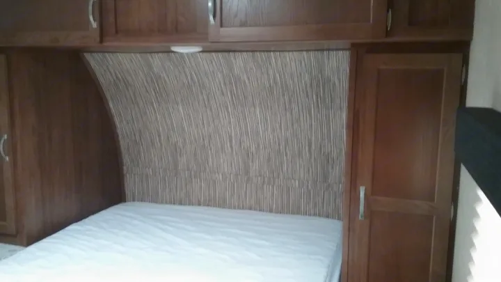 Comfortable RV rental bedroom: clean bed, wood cabinets, curved textured headboard & storage. Your cozy travel sleep spot.. Gulfstream 288ISL 2019