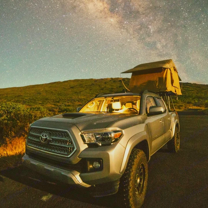 A silver Toyota Tacoma pickup with a raised rooftop tent is illuminated under a dazzling Milky Way night sky, perfect for an RV rental camping adventure.. toyota tacoma 2023