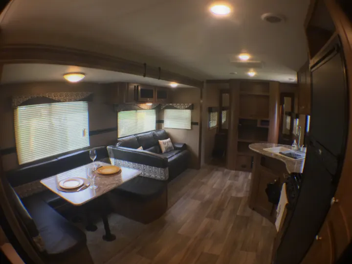 Spacious RV rental interior featuring a dining booth, comfy sofa, and functional kitchen area with sink and fridge.. Dutchmen Aspen Trail 2018