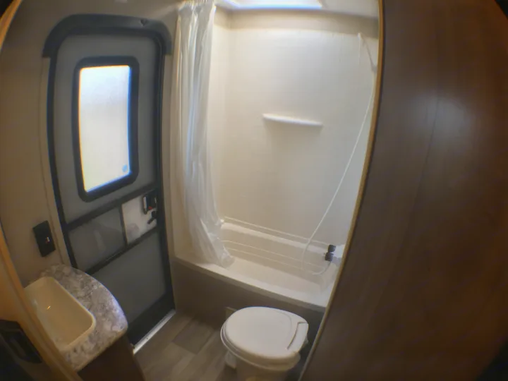 Clean RV rental bathroom with shower, toilet, sink, and door, designed for compact comfort on the road.. Dutchmen Aspen Trail 2018