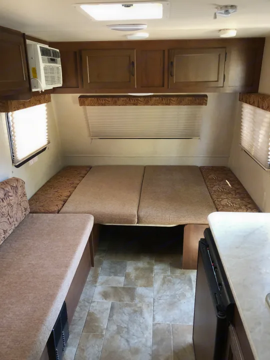 RV rental interior: dinette converts to bed, with overhead cabinets, windows with blinds, AC unit, and tiled floor.. Jayco Jay Flight SLX 2015