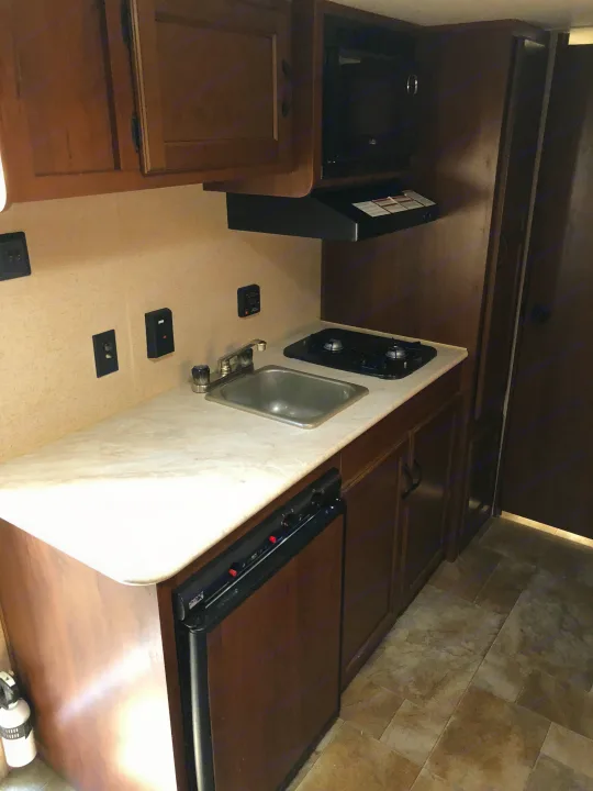 Compact RV rental kitchen: shows a sink, two-burner stove, microwave, and small refrigerator under wooden cabinets.. Jayco Jay Flight SLX 2015