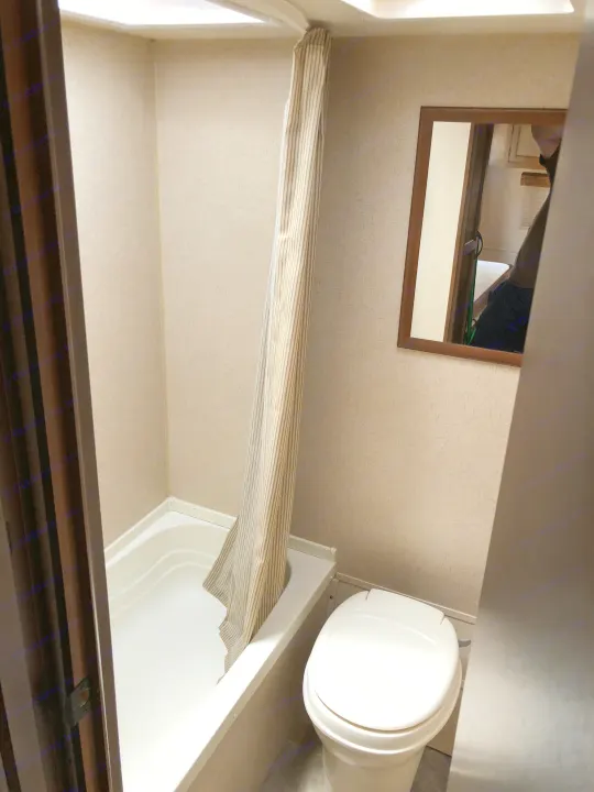 Inside an RV rental, a small bathroom features a white bathtub/shower with a striped curtain, a white toilet, and a mirror.. Jayco Jay Flight SLX 2015