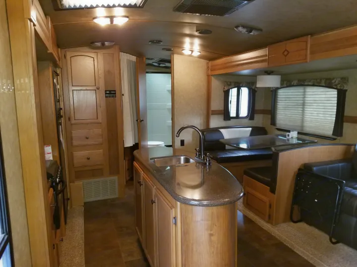 Step inside this rv rental, revealing a kitchen island, a cozy dinette, and bathroom access. Enjoy travel comfort.. Crossroads Sunset Trail 2015
