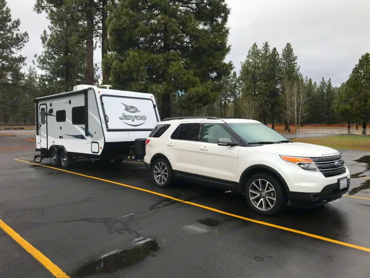 White Ford Explorer SUV towing a Jayco travel trailer (RV rental) in a wet parking lot. Ready for adventure!. Jayco Jay Feather 2017