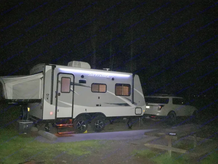 Nighttime view of a Jay Feather RV rental parked at a dark campsite, its exterior lights glowing.. Jayco Jay Feather 2017
