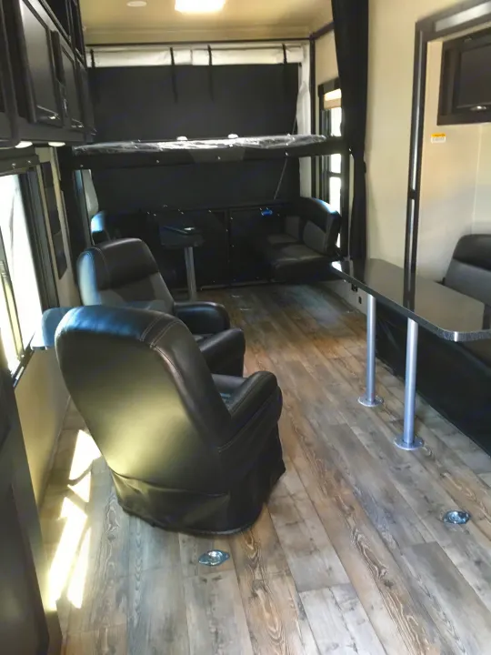 RV rental interior: spacious living area with dark leather chairs, dining table, and a fold-up bunk bed over dark couches.. Genesis Supreme Rv 37GS Toy Hauler 2017