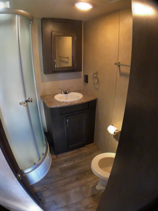 Compact RV rental bathroom offers a curved shower, vanity, sink, mirror, and toilet for essential comfort on the road.. Forest River Evo 2017