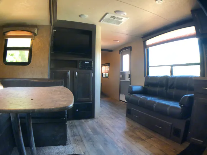Spacious RV rental interior with a dining table & booth, black leather sofa, entertainment center, and wood-look flooring.. Forest River Evo 2017