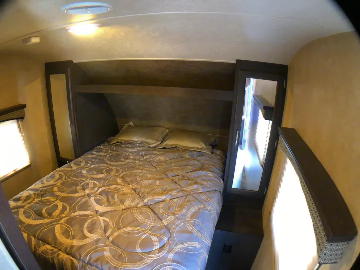 Cozy RV rental bedroom showcasing a comfy bed with patterned comforter, overhead storage, and mirrored cabinets.. Forest River Evo 2017