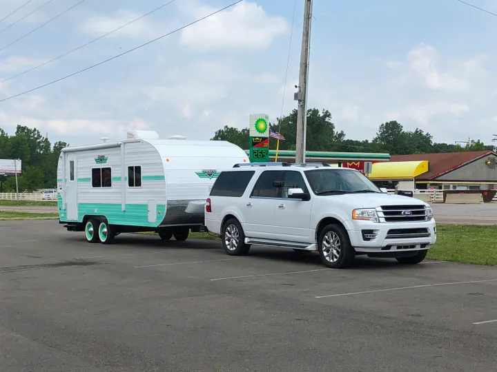 White SUV towing a distinctive retro-style travel trailer, often sought as an RV rental for camping adventures.. Riverside Rv 189R Retro 2018