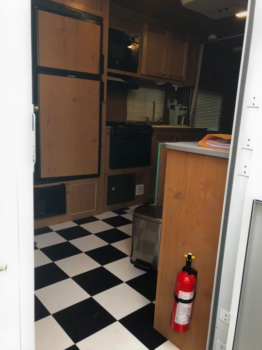 RV rental interior: full kitchen with Dometic fridge, microwave, stove, checkered floor, and fire extinguisher for safety.. Riverside Rv 189R Retro 2018