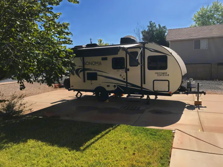 A cream-colored Sonoma Freedom Edition travel trailer, likely an RV rental, parked on a sunny concrete driveway with a house in the background.. Forest River Forester 2017