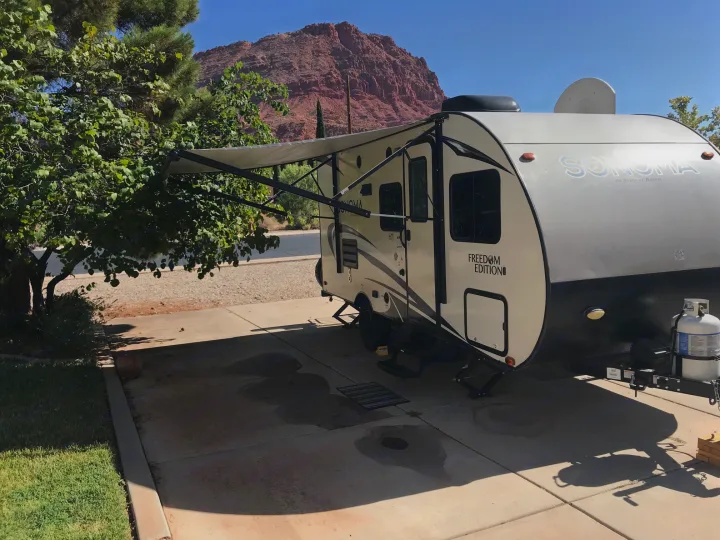 An RV rental with its awning extended is parked on a sunny day, backed by majestic red rock mountains.. Forest River Forester 2017