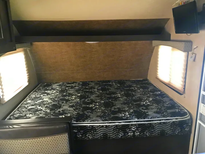 Inside an RV rental: a large bed with patterned mattress, side windows with blinds, overhead storage, and a wall-mounted TV.. Forest River Forester 2017