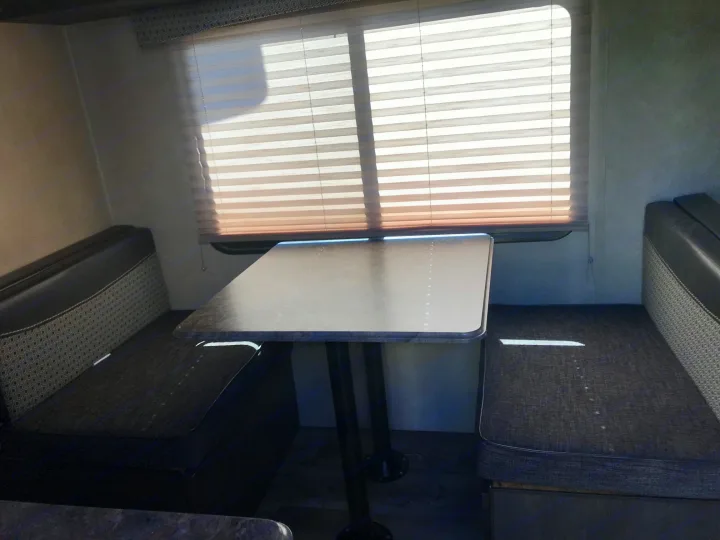 Bright RV rental interior: dinette with grey table, patterned bench seats by a sunlit window.. Forest River Forester 2017