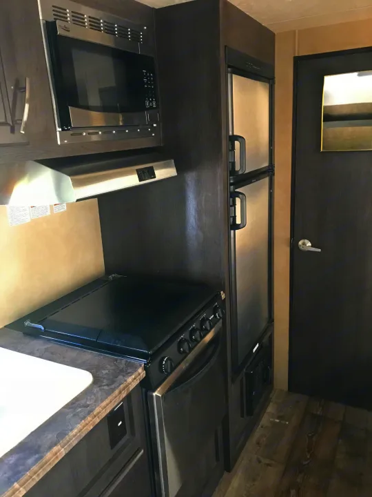 Inside a modern RV rental: sleek kitchen featuring a microwave, stove, oven, and refrigerator. Ready for adventure!. Forest River Forester 2017