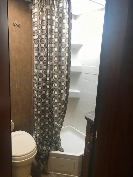 RV rental bathroom features: compact toilet, patterned shower curtain, and functional shower stall with a small vanity.. Jayco Jay Feather 2017