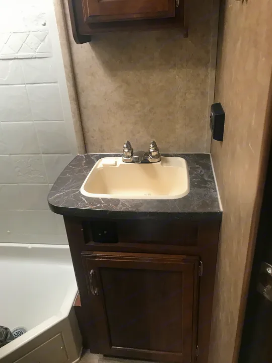 RV rental bathroom: dark vanity, marble-look counter, cream sink, chrome faucet, and partial white tiled shower.. Jayco Jay Feather 2017