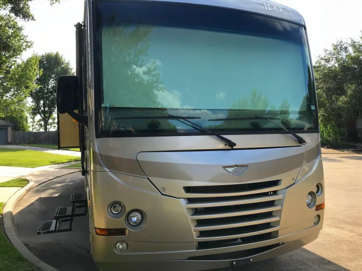 Front of a large, light-colored motorhome, perfect for an RV rental. It's parked on a paved driveway with entry steps down.. Fleetwood Class A 2015