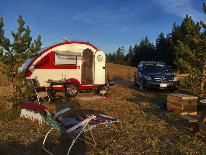 RV rental setup: A red and white teardrop camper and black SUV are parked in a sunny field, ready for outdoor camping leisure.. T@B Q Floorplan Maxx Package 2016