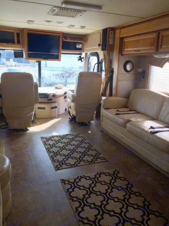 Spacious RV rental interior featuring light leather seating, flat-screen TV, and decorative rugs. View outside shows parked bikes.. Fleetwood Discovery 2005