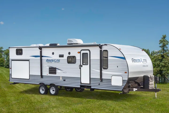This white and gray Ameri-Lite travel trailer, perfect for an RV rental, sits on a grassy field under a blue sky.. Jayco Sport 2019