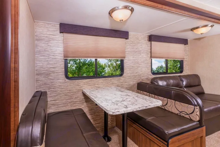 RV rental dinette featuring a modern marble-look table, plush seating, and large windows revealing green trees outside.. kz connect 302 2021