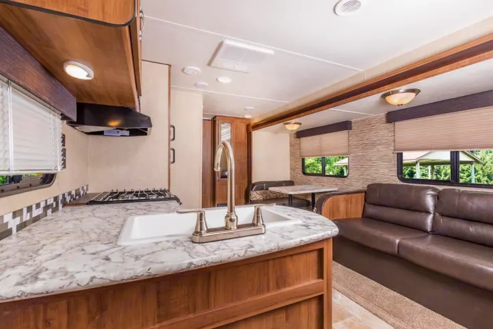 Spacious RV rental interior featuring a modern kitchen with sink & stove, dining booth, and comfortable sofa.. kz connect 302 2021