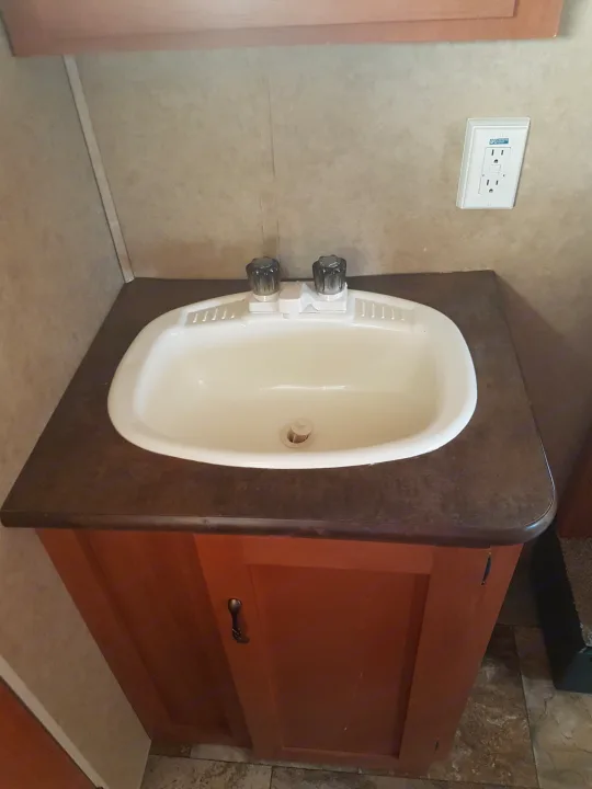 Inside an RV rental: a light-colored bathroom sink, dark countertop, and wood cabinet with a wall outlet.. Grey wolf Other 2015