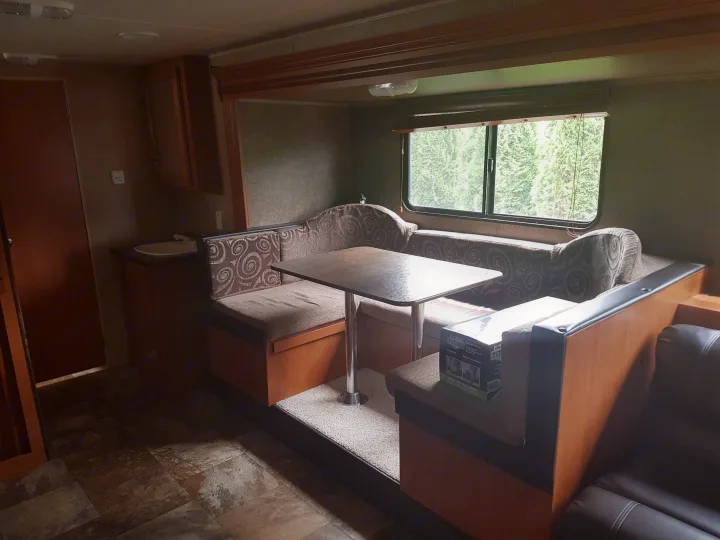 RV rental interior: dinette with table and benches, kitchen counter with sink, and window revealing lush trees.. Grey wolf Other 2015