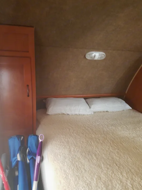 Inside an RV rental: a compact bedroom with a fluffy bed, two pillows, a wooden cabinet, and cleaning tools visible.. Grey wolf Other 2015