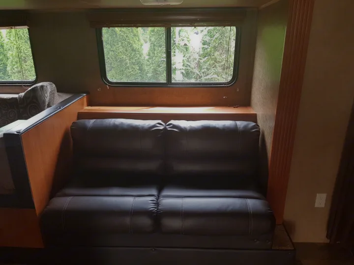 Inside a cozy RV rental: a dark leather sofa, wood accents, and large windows revealing green outdoor trees.. Grey wolf Other 2015