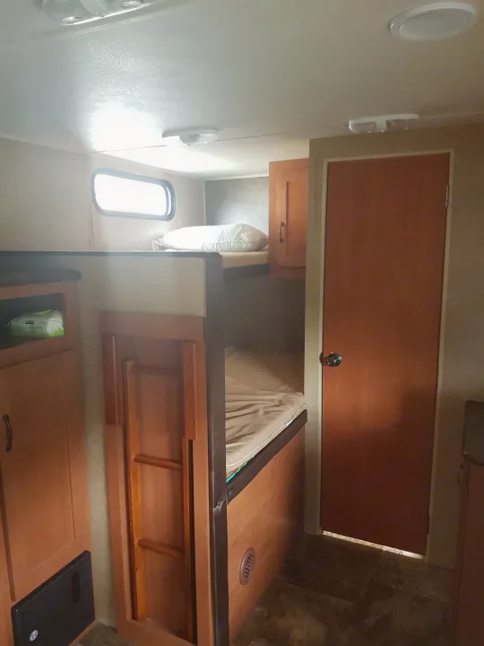 Inside an RV rental: two bunk beds with a ladder, storage, and a wooden door create a practical sleeping area.. Grey wolf Other 2015