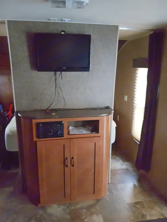 Interior view of an RV rental showing a mounted TV above a wooden entertainment cabinet with audio system.. Grey wolf Other 2015