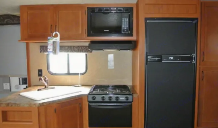 RV rental kitchen view: wood cabinets, black microwave, stove, and fridge. Includes a sink & countertop.. Grey wolf Other 2015